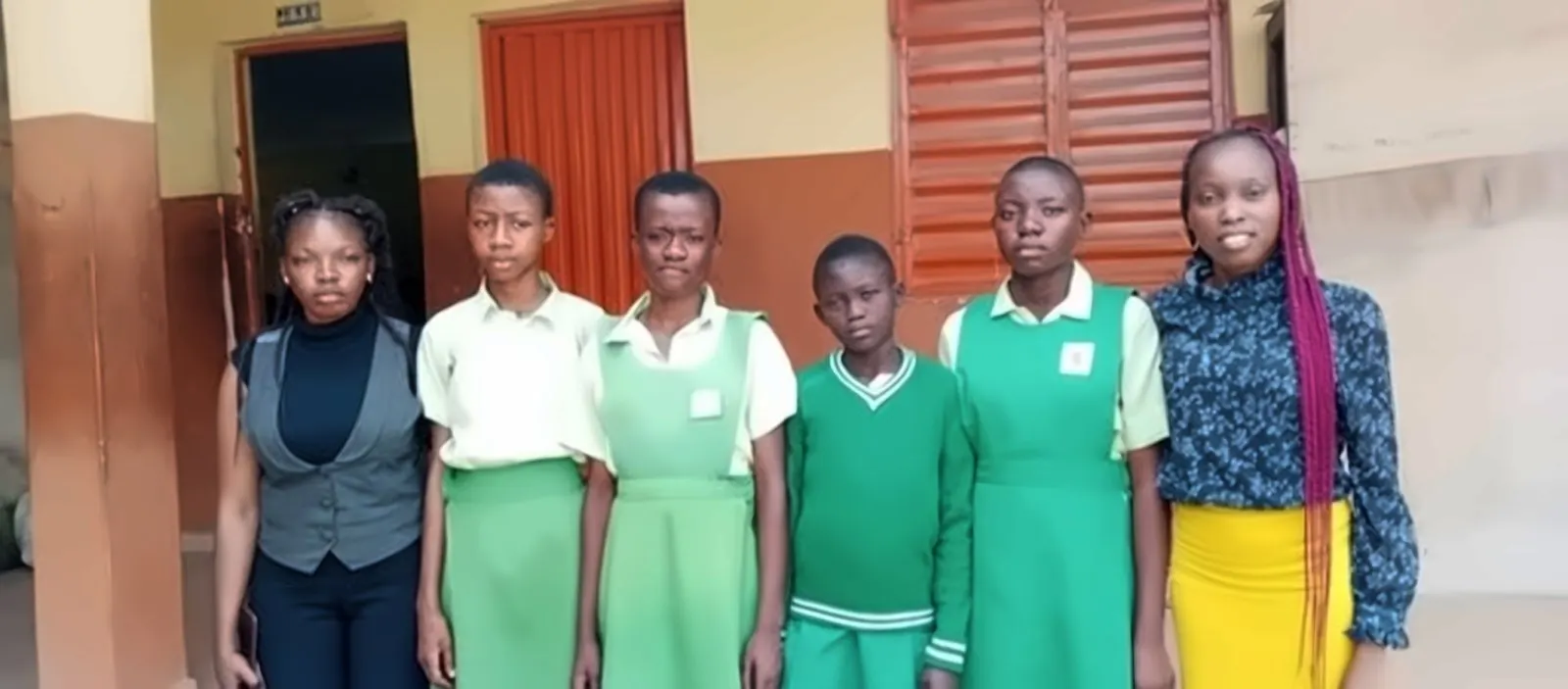 Volunteers standing with students in green uniforms